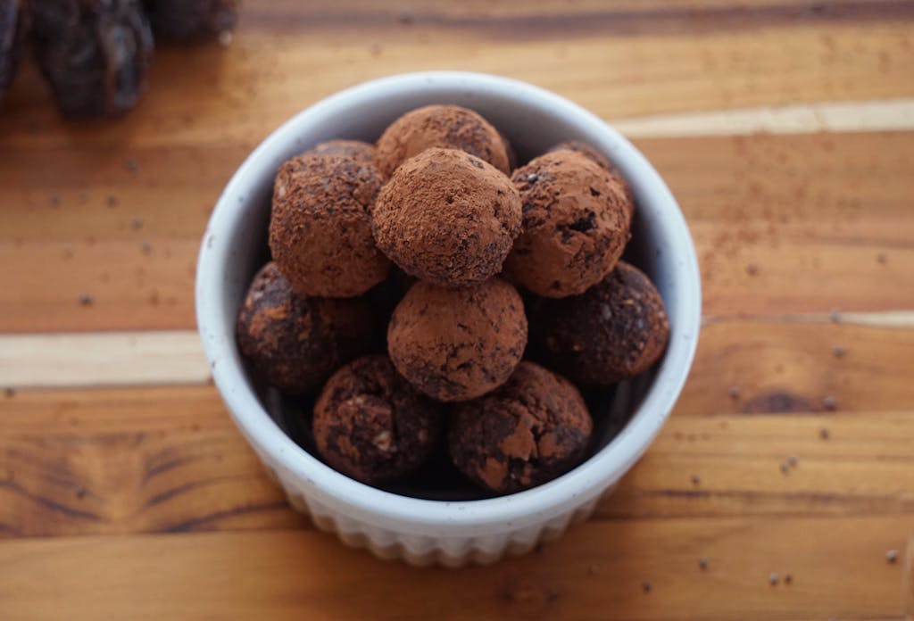 A bowl of homemade chocolate truffles dusted with cacao powder on a rustic wooden surface.