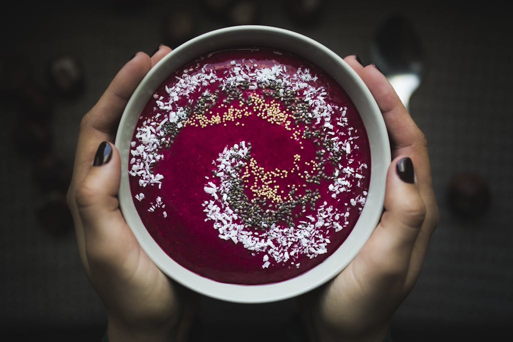A vibrant berry bowl topped with coconut flakes and seeds held in hands.